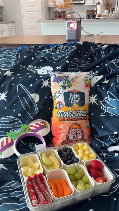 Instagram post by @thedailyammie for LesserEvil. Caption reads: @lesserevilsnacks Space Balls in collaboration....