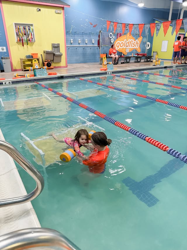 Instagram post by @themodernlatinamama for Goldfish Swim School. Caption reads: [...] face in the water. - #swimlessons....