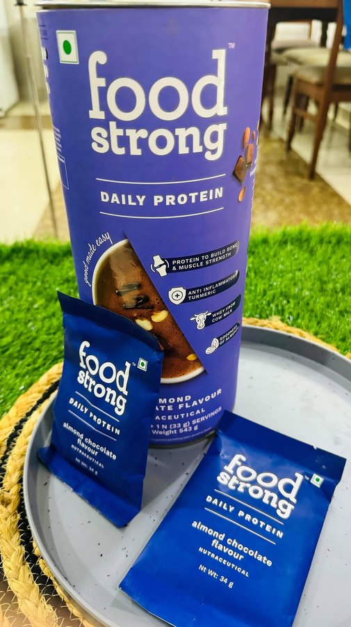 Instagram post by @fitnessbyfood_official for foodstrong. Caption reads: Foodstrong Daily Protein Real Almond Chocolate,....