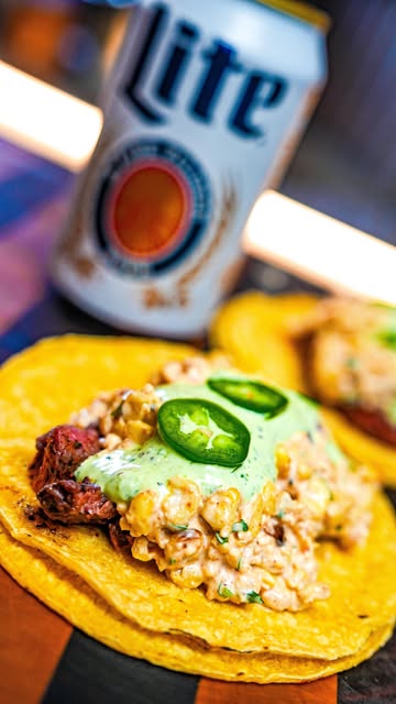Instagram post by @tfti.bbq for Miller Lite. Caption reads: 𝙀𝙇𝙊𝙏𝙀 𝙎𝙏𝙍𝙀𝙀𝙏 𝘾𝙊𝙍𝙉 𝙏𝘼𝘾𝙊𝙎
w/....