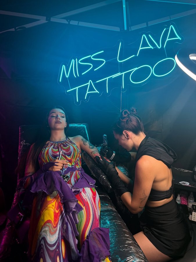 Instagram post by @miss.lava.tattoo for EMALLA Official. Caption reads: Would you get a tattoo at a music festival?!....